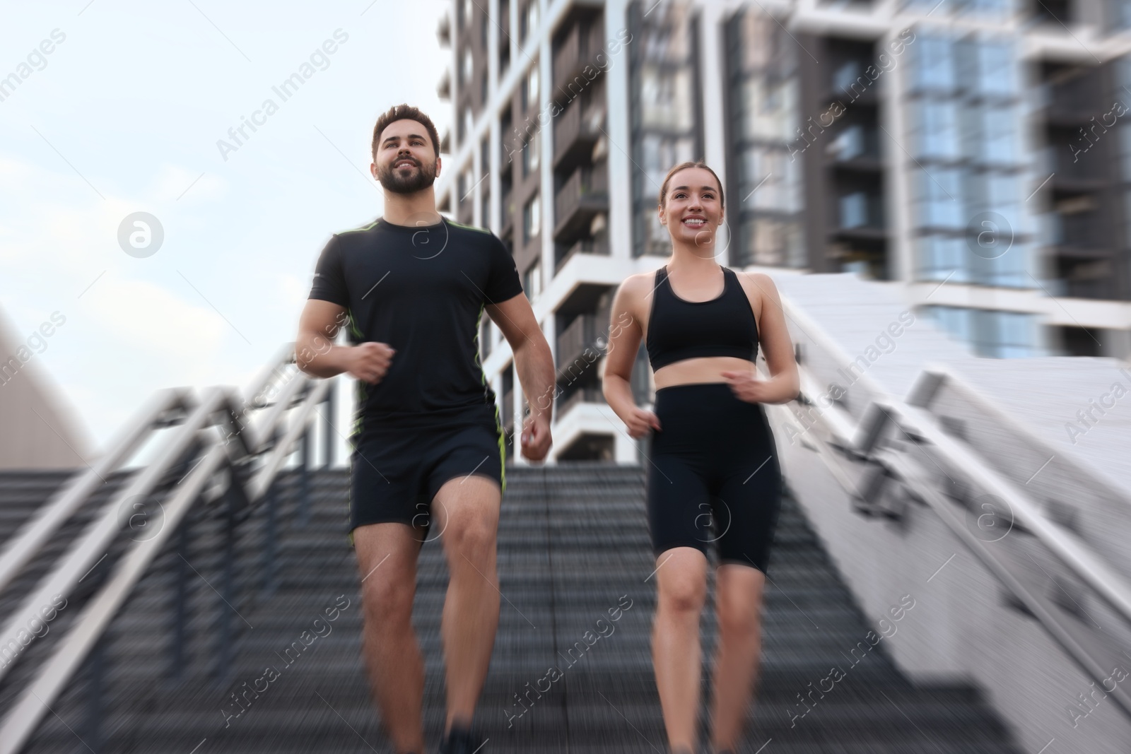 Woman and man in sportswear running down on stairs outdoors, motion blue effect. Low angle view Image of Woman and man in sportswear running down on stairs outdoors, motion blue effect. Low angle view
