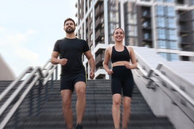 Image of Woman and man in sportswear running down on stairs outdoors, motion blue effect. Low angle view