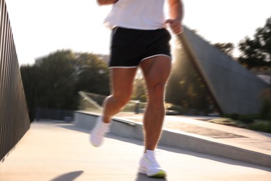 Image of Man in sportswear running outdoors on sunny morning, motion blue effect