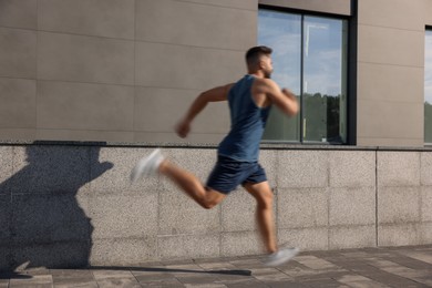 Image of Man in sportswear running near building outdoors, motion blue effect