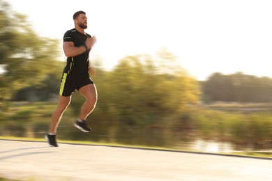 Image of Man in sportswear running outdoors on sunny morning, motion blue effect