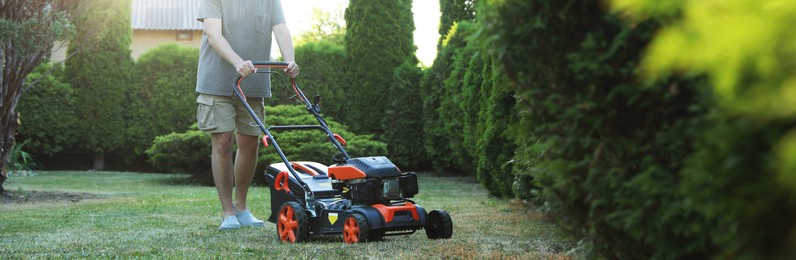 Photo of Man cutting green grass with lawn mower in garden, closeup
