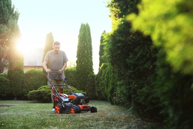 Photo of Man cutting green grass with lawn mower in garden