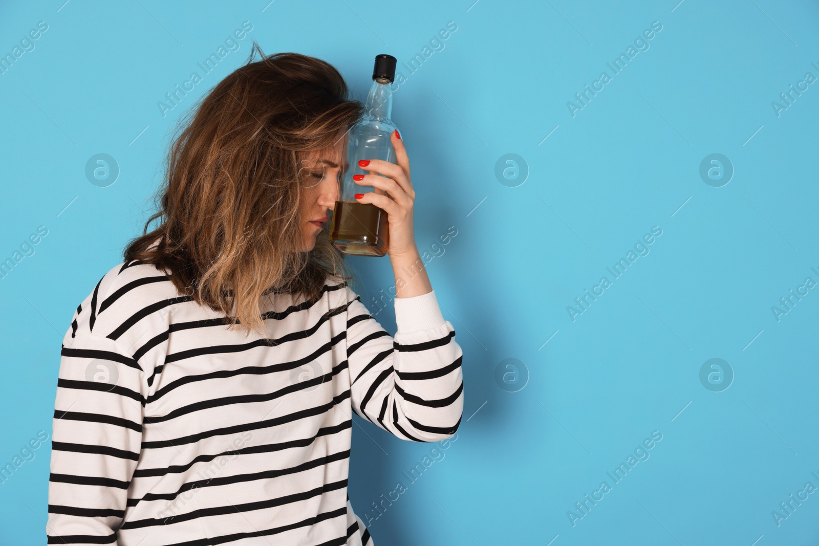 Woman with bottle of alcoholic drink suffering from hangover on light blue background. Space for text Photo of Woman with bottle of alcoholic drink suffering from hangover on light blue background. Space for text