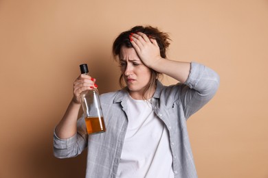 Photo of Woman with bottle of alcoholic drink suffering from hangover on beige background