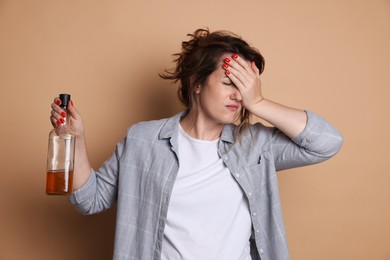 Photo of Woman with bottle of alcoholic drink suffering from hangover on beige background