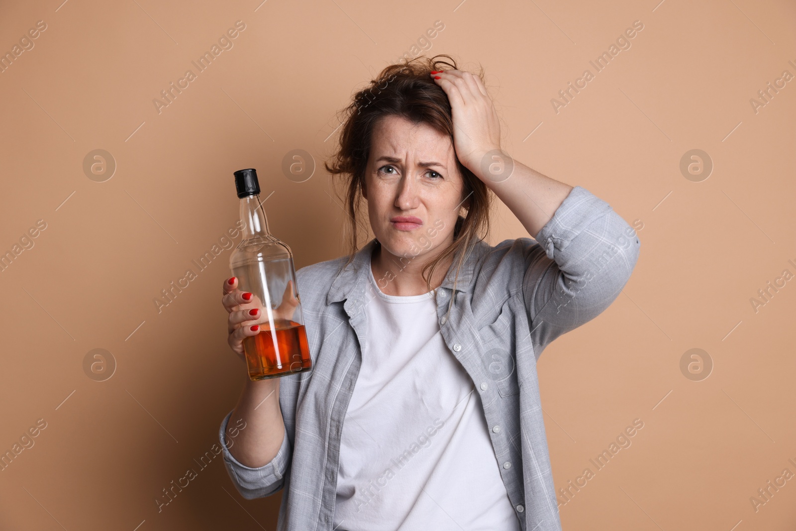 Photo of Woman with bottle of alcoholic drink suffering from hangover on beige background