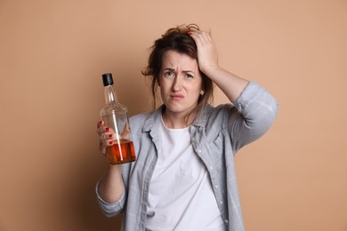 Photo of Woman with bottle of alcoholic drink suffering from hangover on beige background