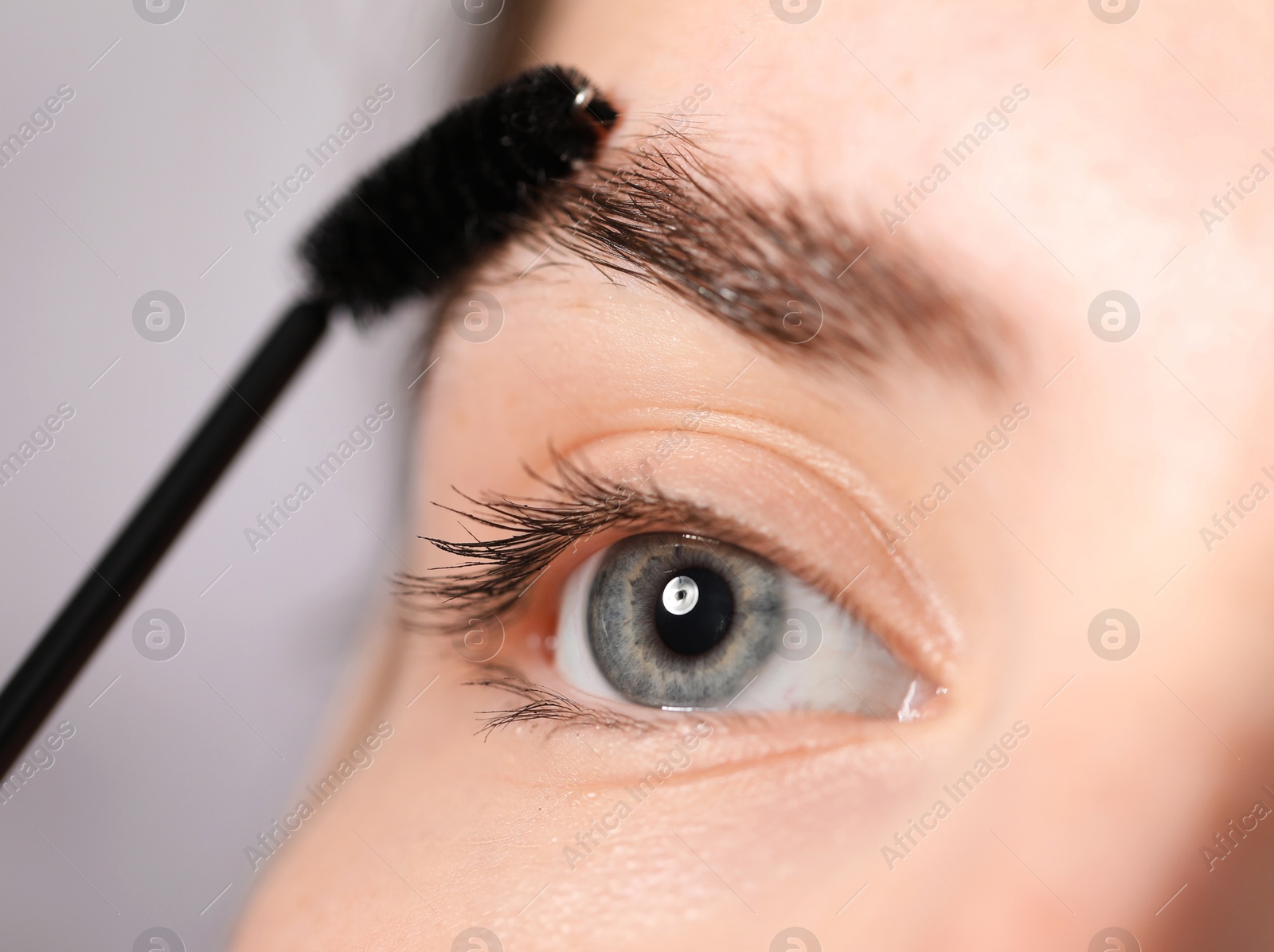 Photo of Young woman brushing her eyebrow with spoolie on light grey background, closeup