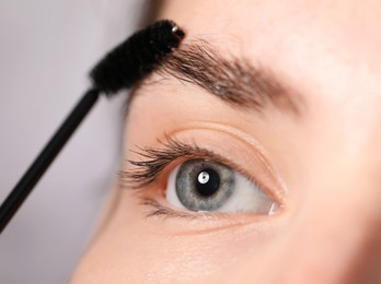 Photo of Young woman brushing her eyebrow with spoolie on light grey background, closeup