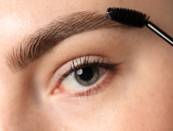 Photo of Young woman brushing her eyebrow with spoolie, closeup
