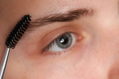 Photo of Young woman brushing her eyebrow with spoolie, closeup