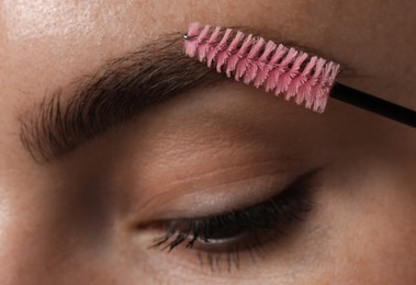 Photo of Young woman brushing her eyebrow with spoolie, closeup