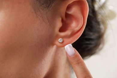Photo of Woman pointing at her stylish earring on light background, closeup