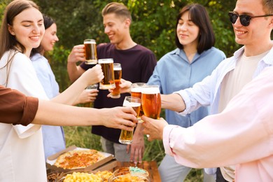 Photo of Group of happy friends clinking glasses of beer outdoors, selective focus