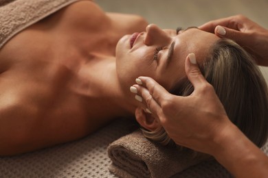 Photo of Beautiful woman receiving facial massage on couch in spa salon, closeup