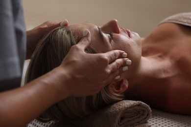 Photo of Beautiful woman receiving facial massage on couch in spa salon, closeup