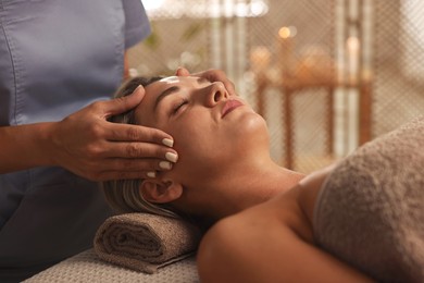 Photo of Beautiful woman receiving facial massage on couch in spa salon, closeup