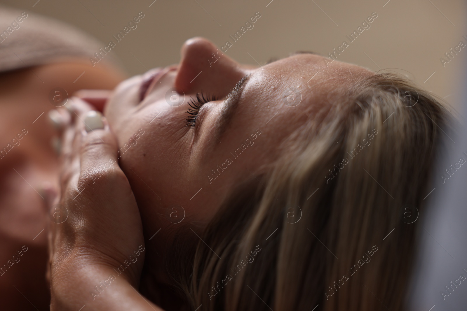 Beautiful woman receiving facial massage on blurred beige background, closeup Photo of Beautiful woman receiving facial massage on blurred beige background, closeup
