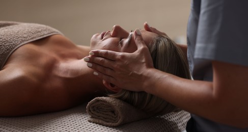 Photo of Beautiful woman receiving facial massage on couch in spa salon, closeup