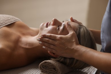 Photo of Beautiful woman receiving facial massage on couch in spa salon, closeup