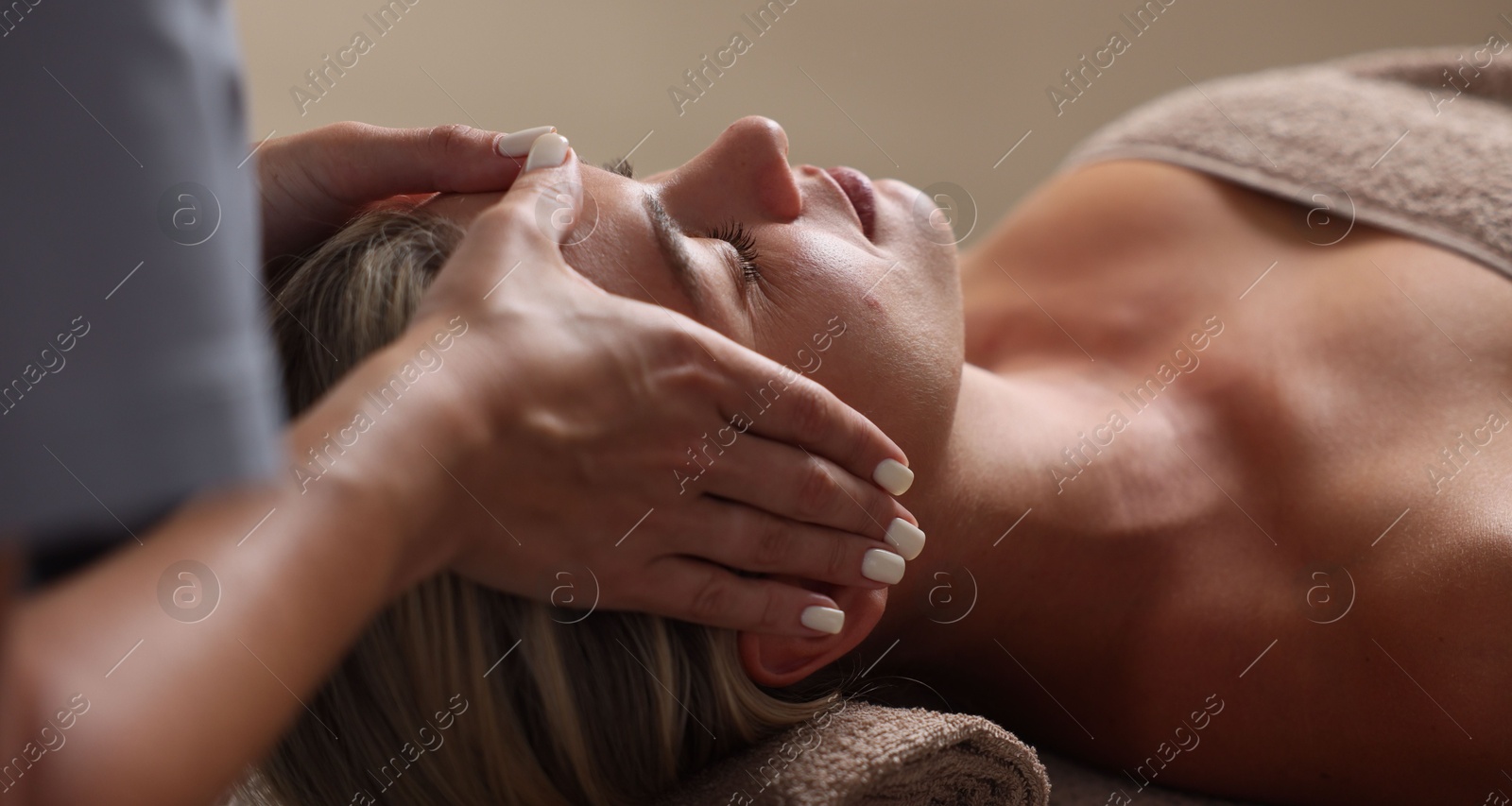 Beautiful woman receiving facial massage on blurred beige background, closeup Photo of Beautiful woman receiving facial massage on blurred beige background, closeup