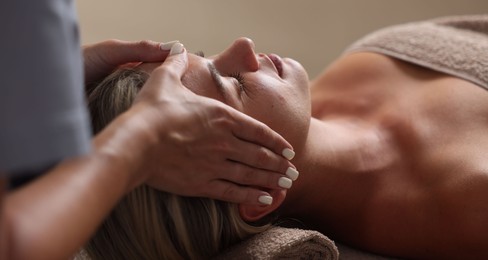 Photo of Beautiful woman receiving facial massage on blurred beige background, closeup