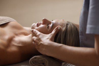 Photo of Beautiful woman receiving facial massage on blurred beige background, closeup