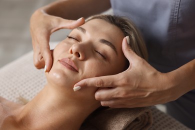 Photo of Beautiful woman receiving facial massage on couch in spa salon, closeup
