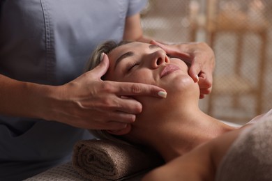 Photo of Beautiful woman receiving facial massage on couch in spa salon, closeup