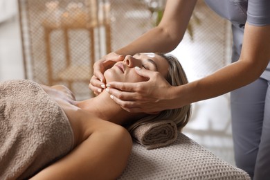 Photo of Beautiful woman receiving facial massage on couch in spa salon, closeup
