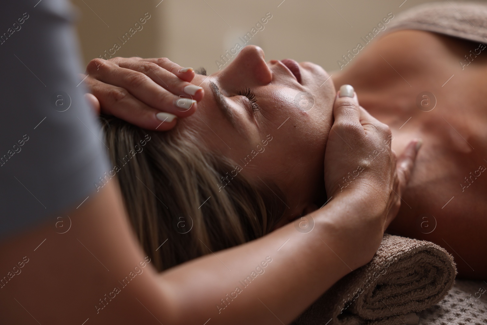 Beautiful woman receiving facial massage on blurred beige background, closeup Photo of Beautiful woman receiving facial massage on blurred beige background, closeup