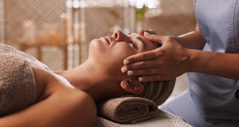 Photo of Beautiful woman receiving facial massage on couch in spa salon, closeup
