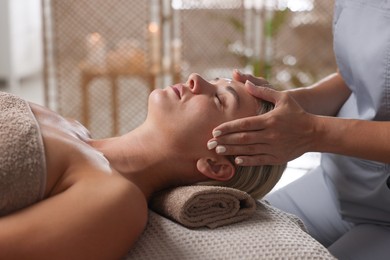 Photo of Beautiful woman receiving facial massage on couch in spa salon, closeup