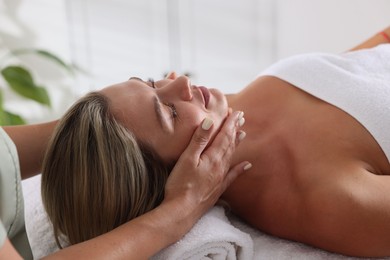 Photo of Beautiful woman receiving facial massage on couch in spa salon, closeup