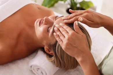 Photo of Beautiful woman receiving facial massage on couch in spa salon, closeup