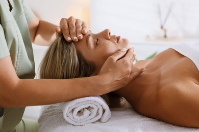 Photo of Beautiful woman receiving facial massage on couch in spa salon, closeup