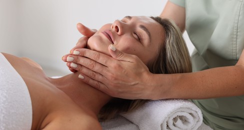 Photo of Beautiful woman receiving facial massage on couch indoors, closeup