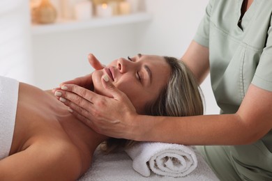 Photo of Beautiful woman receiving facial massage on couch in spa salon, closeup