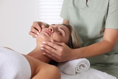 Photo of Beautiful woman receiving facial massage on couch in spa salon, closeup