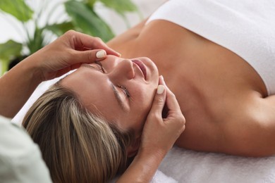 Photo of Beautiful woman receiving facial massage on couch indoors, closeup
