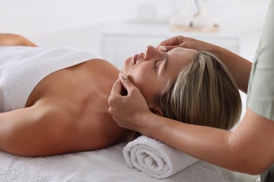 Photo of Beautiful woman receiving facial massage on couch indoors, closeup
