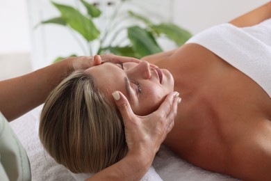 Photo of Beautiful woman receiving facial massage on couch indoors, closeup