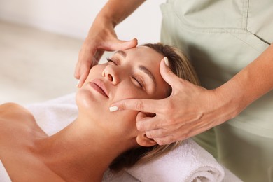 Photo of Beautiful woman receiving facial massage on couch indoors, closeup