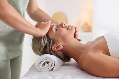 Photo of Beautiful woman receiving facial massage on couch in spa salon, closeup