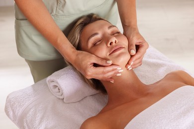 Photo of Beautiful woman receiving facial massage on couch in spa salon, closeup