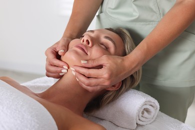Photo of Beautiful woman receiving facial massage on couch in spa salon, closeup