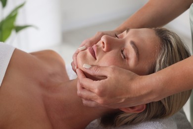Photo of Beautiful woman receiving facial massage indoors, closeup