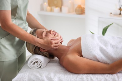 Photo of Beautiful woman receiving facial massage on couch in spa salon, closeup