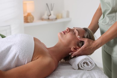 Photo of Beautiful woman receiving facial massage on couch in spa salon, closeup